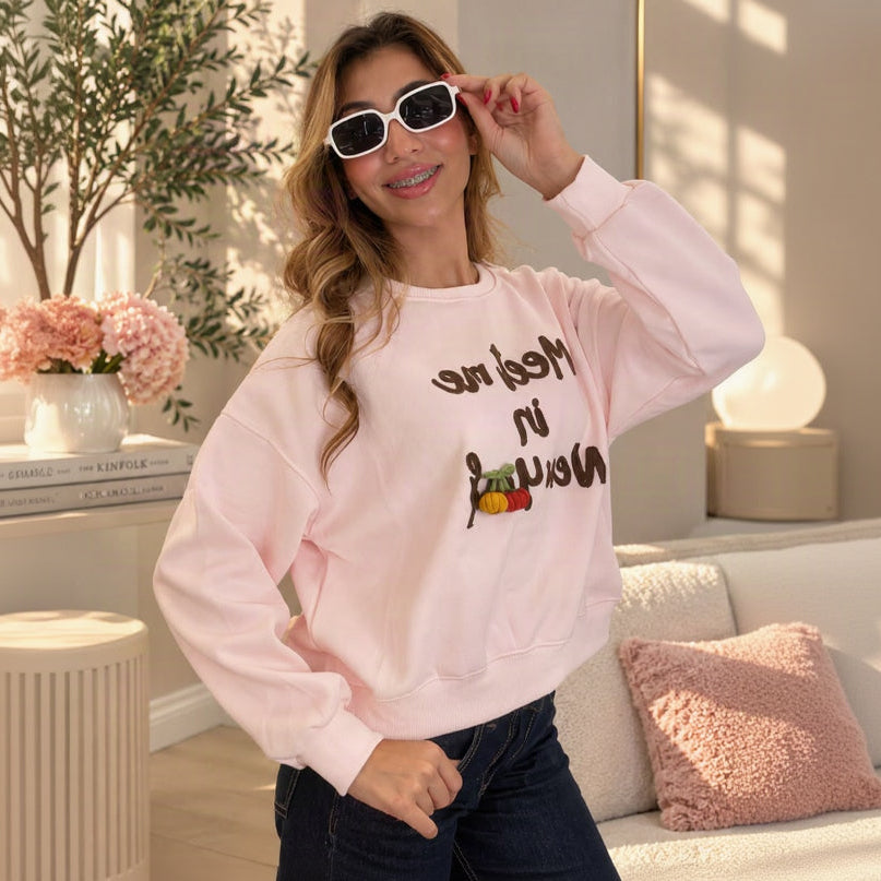 Woman lifting her sunglasses in a pale pink Meet me in New York sweatshirt with brown lettering