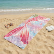 Rose pink mermaid tail beach towel with a pastel scallop scale print on sand