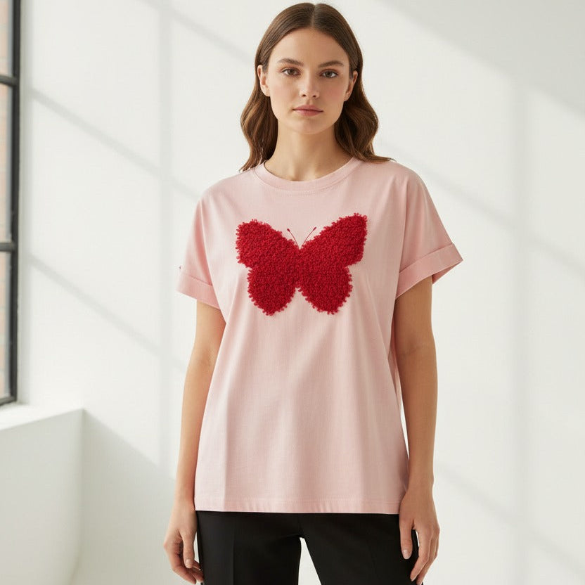 Woman wearing a pink tshirt with a red butterfly design in a minimalistic setting