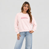 Pale pink sequin letter sweatshirt worn with wide light jeans against a plain grey wall