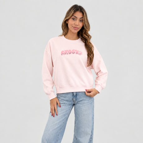 Pale pink sequin letter sweatshirt worn with wide light jeans against a plain grey wall