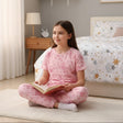 Pink short sleeve pajama set with teddy bear outline print worn cross legged
