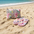 Flip flops and pouch with floral and leopard print design on sand