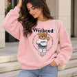 Woman in a pink sweatshirt with a Weekend Vibes Only print and a fuzzy waving teddy bear