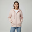 Woman wearing a light pink hoodie and blue jeans on a plain background