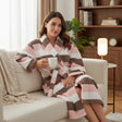 Smiling woman on a cream sofa in a pink, white and brown striped robe with a mug