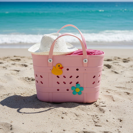 Pink crocs beach bag with a rubber duck and flowers on the beach, with a hat and towel in it.