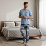Plaid pyjama set worn holding a mug beside a neatly made bed