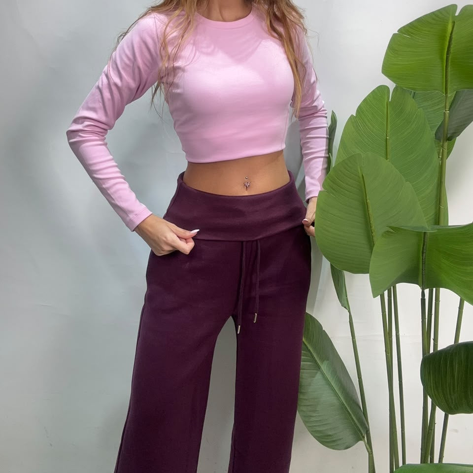 Full length view of plum wide leg sweatpants with one hand on the hip beside a green plant