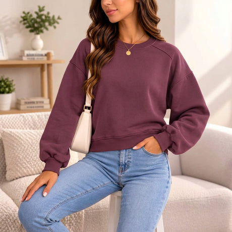 Woman in a plum oversized crew neck sweatshirt with balloon sleeves and a cream shoulder bag
