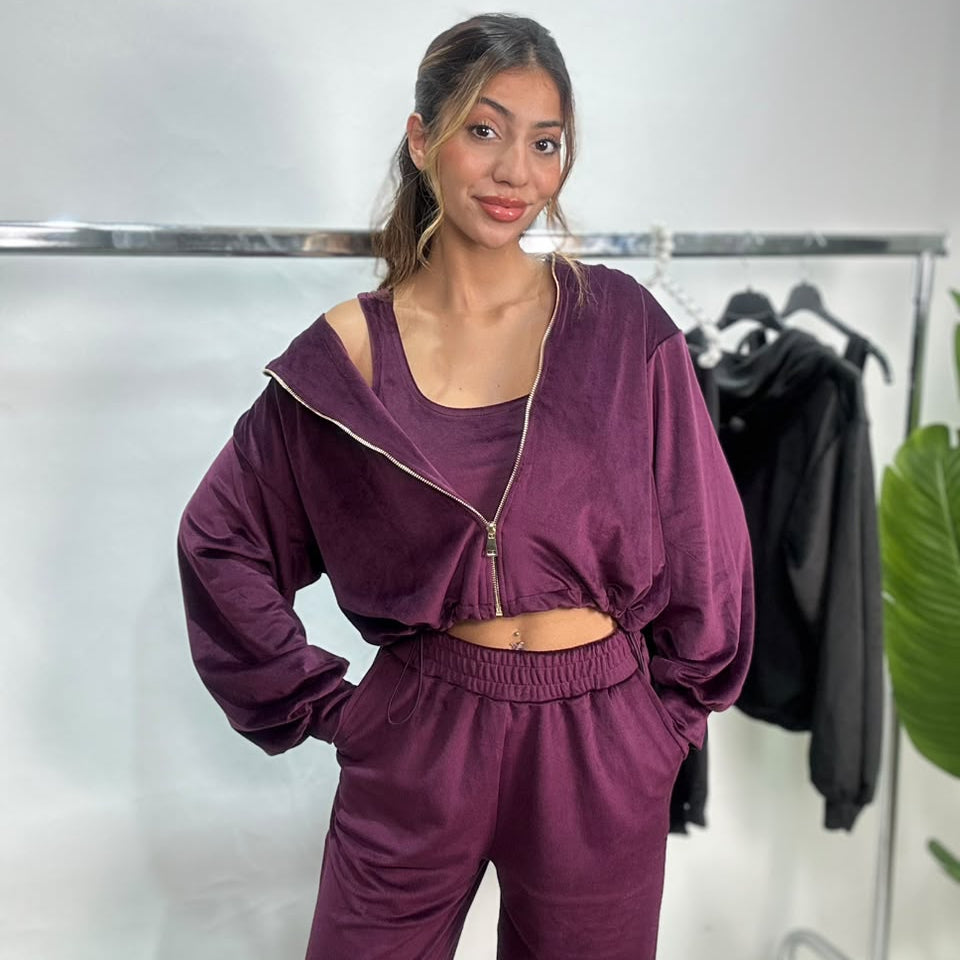 Woman in a plum velvet zip jacket, matching crop top and wide leg pants with hands in pockets