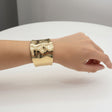 Gold polished wide cuff bracelet on a wrist against a neutral background