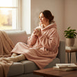 Powder pink hooded blanket with sherpa lined hood and front pocket worn curled up on a sofa