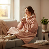Powder pink hooded blanket with sherpa lined hood and front pocket worn curled up on a sofa