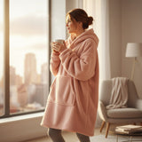 Soft pink hooded blanket worn standing by a bright window holding a warm drink