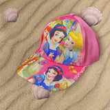 Bright pink girls cap resting on sand, brim and crown covered in colourful cartoon princess artwork