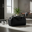 Black duffel bag on a concrete floor with shoes and a plant in the background