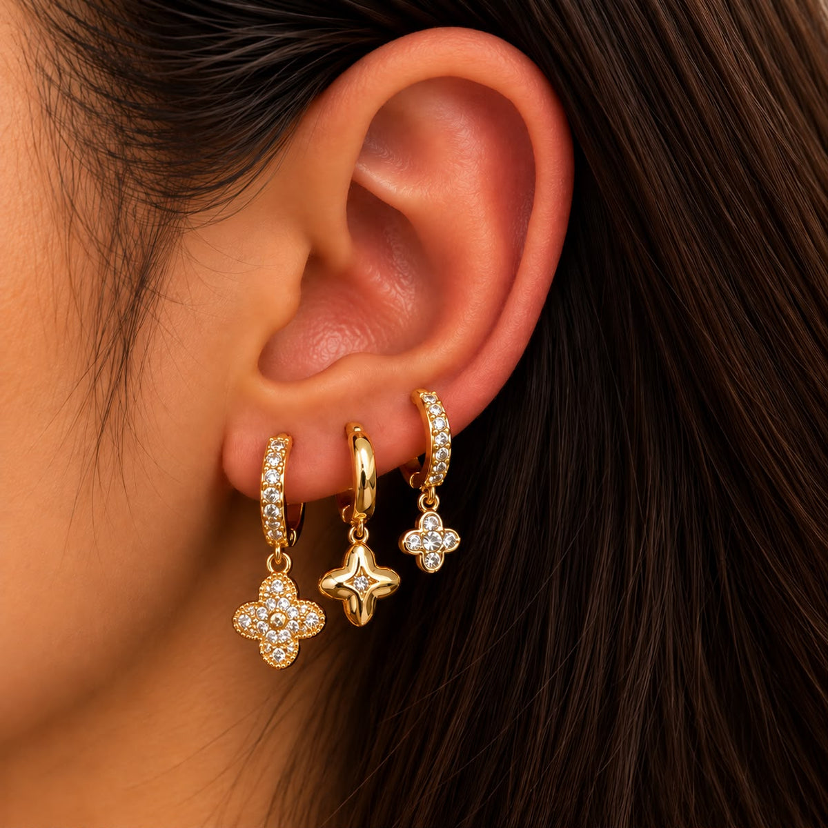 Ear wearing three gold huggies with a crystal clover, a puffed gold clover and a small crystal clover