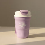 Purple coffee tumbler with white text on a white surface, with stacks of folded clothes in the background.