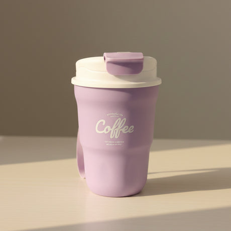 Purple coffee tumbler with white text on a white surface, with stacks of folded clothes in the background.