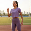 Woman in purple athletic wear standing on a running track with city skyline in the background