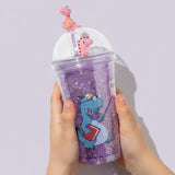 Purple dino glitter cup held in a child's hands against a lilac backdrop