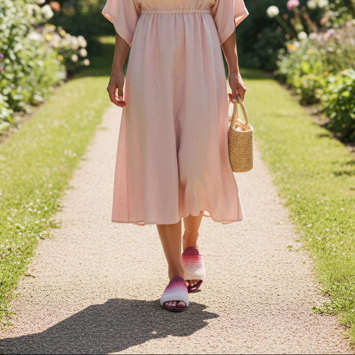 Woman in a pink dress wearing puple handmade slippers walking along a garden path