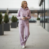 Woman in a purple jogging set walking outdoors holding a coffee cup