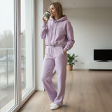 Woman in a pink hoodie and sweatpants standing by a window in a modern living room