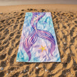 Colorful mermaid tail towel on a sandy beach with ocean waves in the background