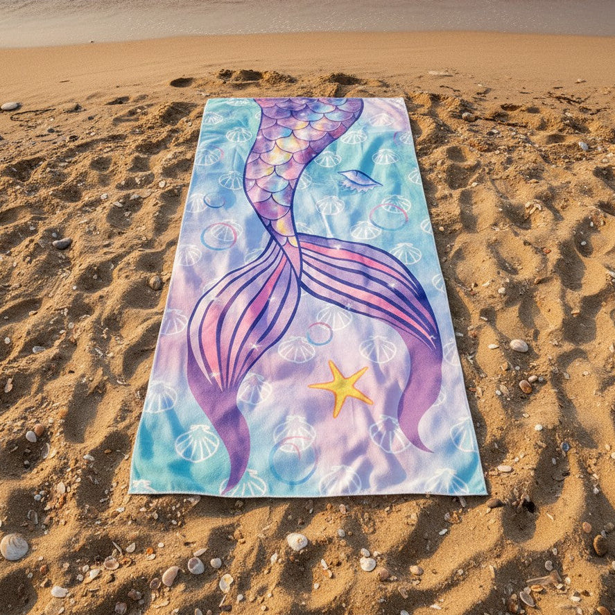 Colorful mermaid tail towel on a sandy beach with ocean waves in the background