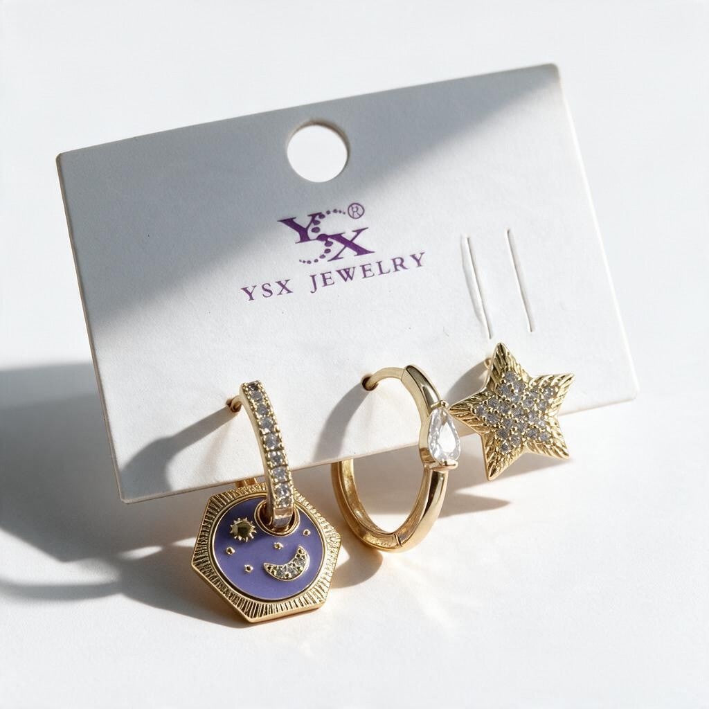 Three gold single earrings on a card with a purple moon charm drop, a crystal teardrop hoop and a pave star stud