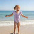 Girl wearing a purple striped onepiece swimsuit with ruffled cap sleeves on the beach