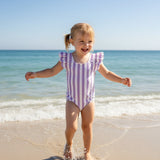 Girl wearing a purple striped onepiece swimsuit with ruffled cap sleeves on the beach