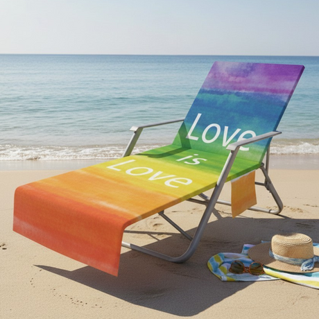 A beach lounge chair on a sandy beach with the ocean in the background. The chair has a colorful rainbow gradient design with the words 'Love is' printed on it.
