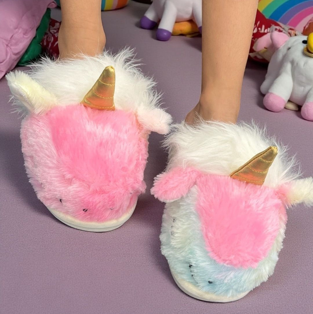 Pink and white unicorn slippers with a gold horn shown on a fluffy rug