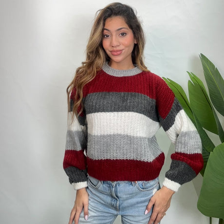 Woman standing in a red, grey and white striped sweater with light jeans by a palm plant