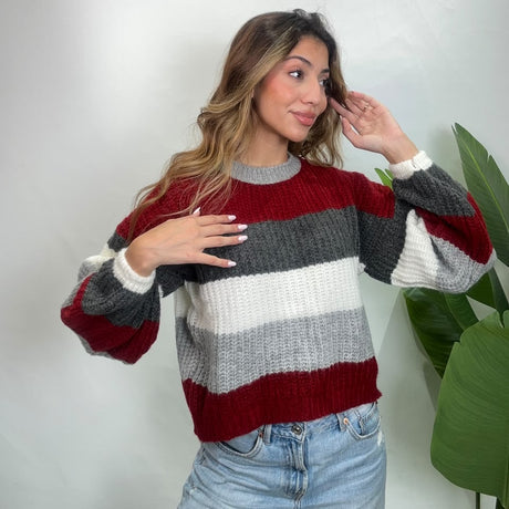 Red and grey colour block knit sweater with a grey crew neck, one hand on her chest