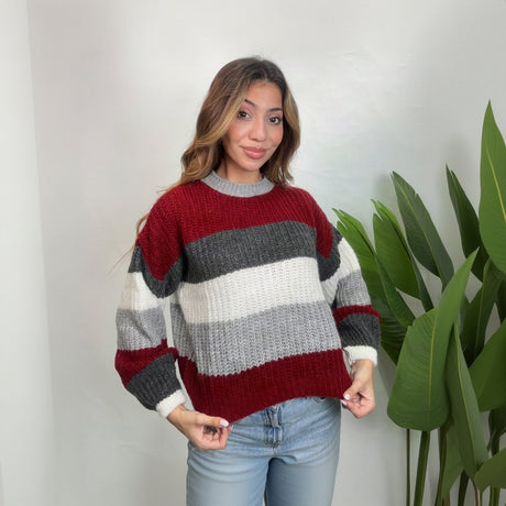 Woman in a red and grey striped chunky sweater with white cuffs, hands at her hem