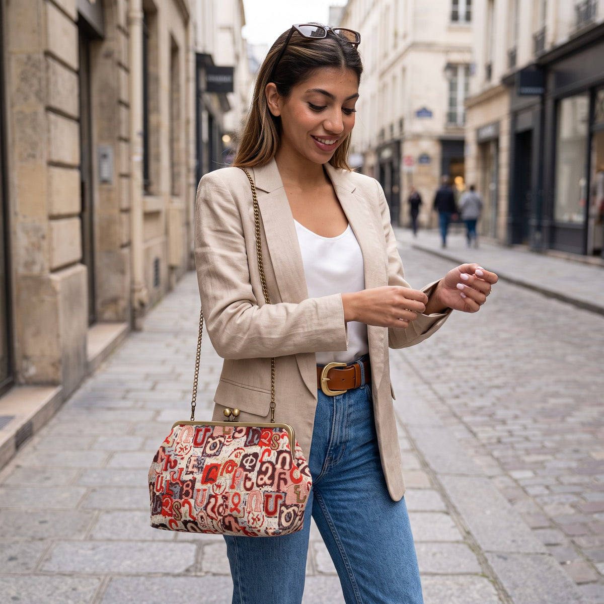 Woman in a beige blazer and jeans carrying a red Armenian letter tapestry bag on a chain
