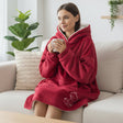 Woman wearing a red hooded blanket sitting on a couch holding a mug.