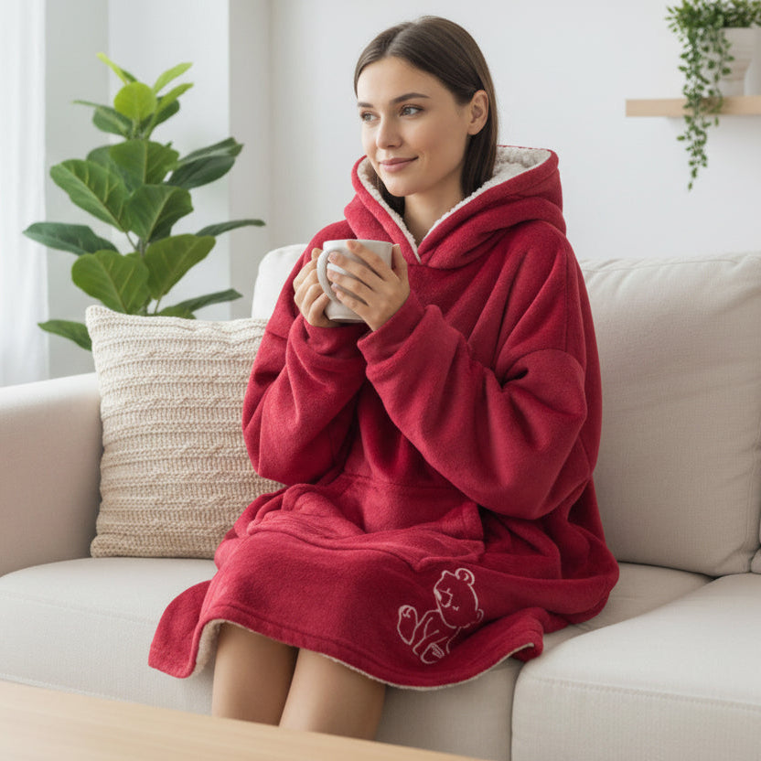 Woman wearing a red hooded blanket sitting on a couch holding a mug.