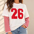 Woman in a white tee with a distressed red 26 print and red striped long sleeves