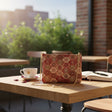 Red medallion tapestry crossbody bag with a gold chain on a table