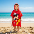 Boy on the beach wearing a red Mickey Mouse poncho towel with a waving Mickey print