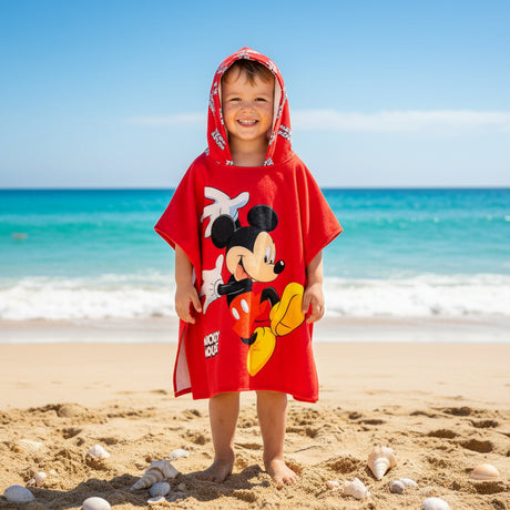Boy on the beach wearing a red Mickey Mouse poncho towel with a waving Mickey print