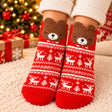 Red Nordic pattern Christmas socks with white reindeer and a fuzzy brown bear face at the cuff