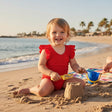 Toddler wearing a red ruffled onepiece swimsuit at the beach