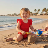Toddler wearing a red ruffled onepiece swimsuit at the beach