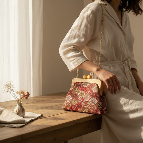 Woman in white linen leaning on a table with the red tapestry bag on her shoulder